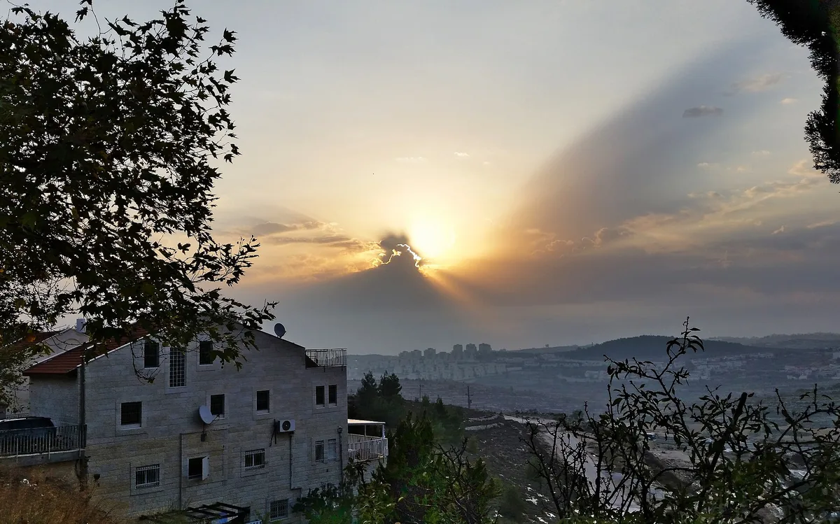 Sunrise over the hills seen from Neve Daniel, with stone houses and trees in the foreground