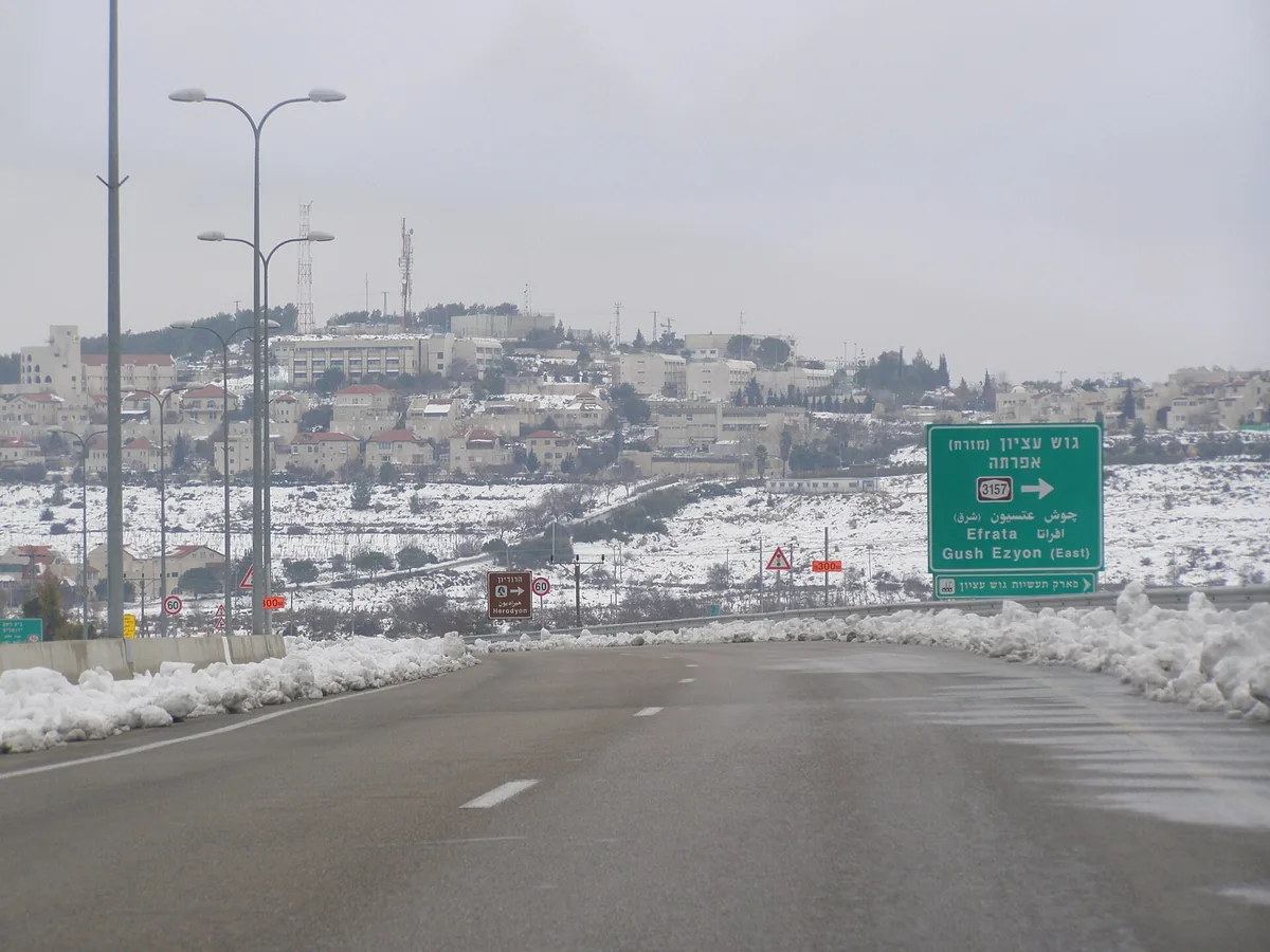 Efrat's houses on the hillside after snowfall, seen from the main road with a road sign