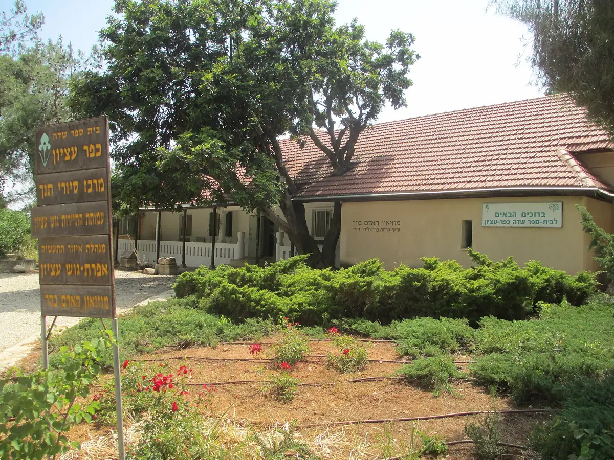 The Kfar Etzion sign by a red-roofed building and a flower bed on the kibbutz
