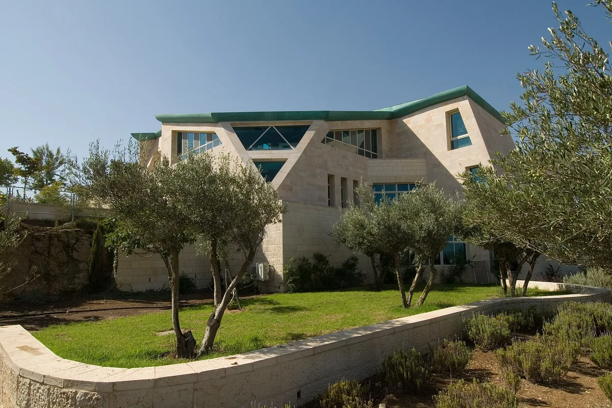 The stone building of the women's beit midrash at Migdal Oz, with olive trees and a lawn in front